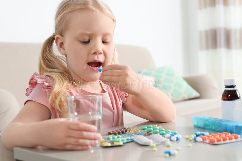 Little child taking pill at table. Danger of medicament intoxication stock photos