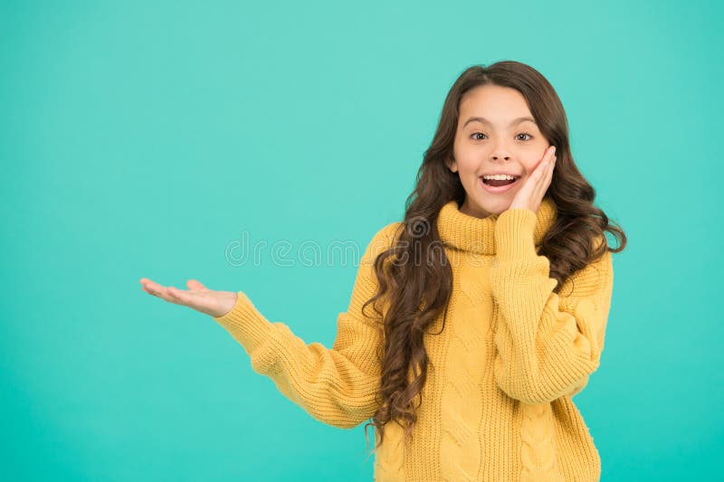 Little child wear snuggly sweater with style. Surprised small girl long hair. knitting for kids. Little girl on blue