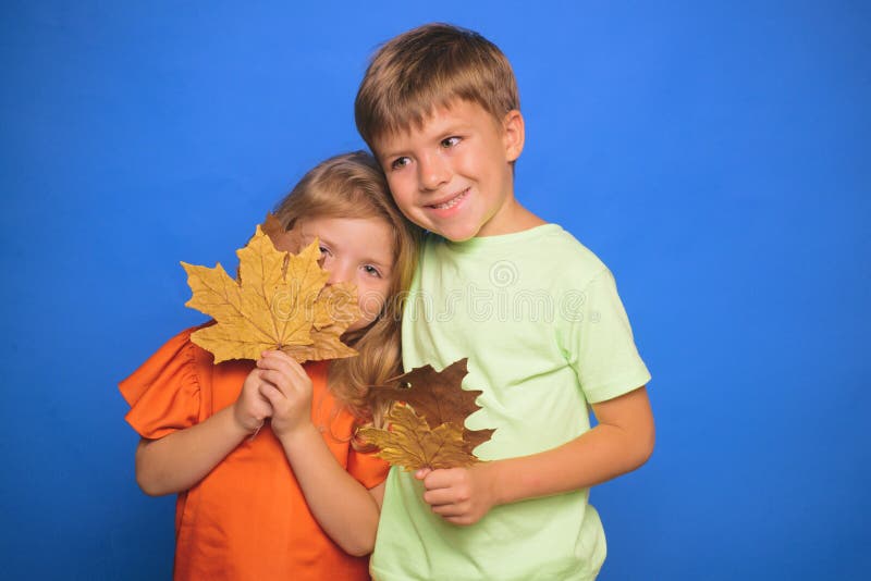 Little children in autumn playing with leaves on autumn colour background. Little boy and girl in seasonal clothes with stock image Little children in autumn playing with leaves on autumn colour background. Little boy and girl in seasonal clothes with stock image