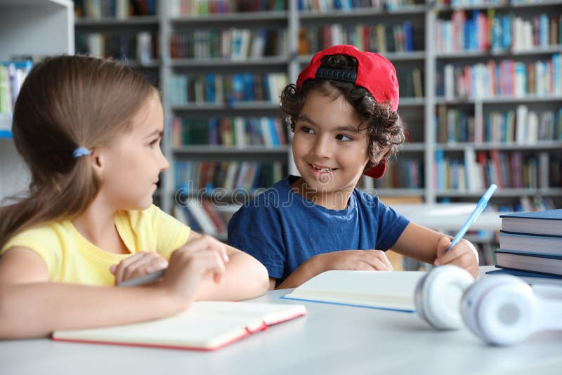 Little children writing at table with books in library room
