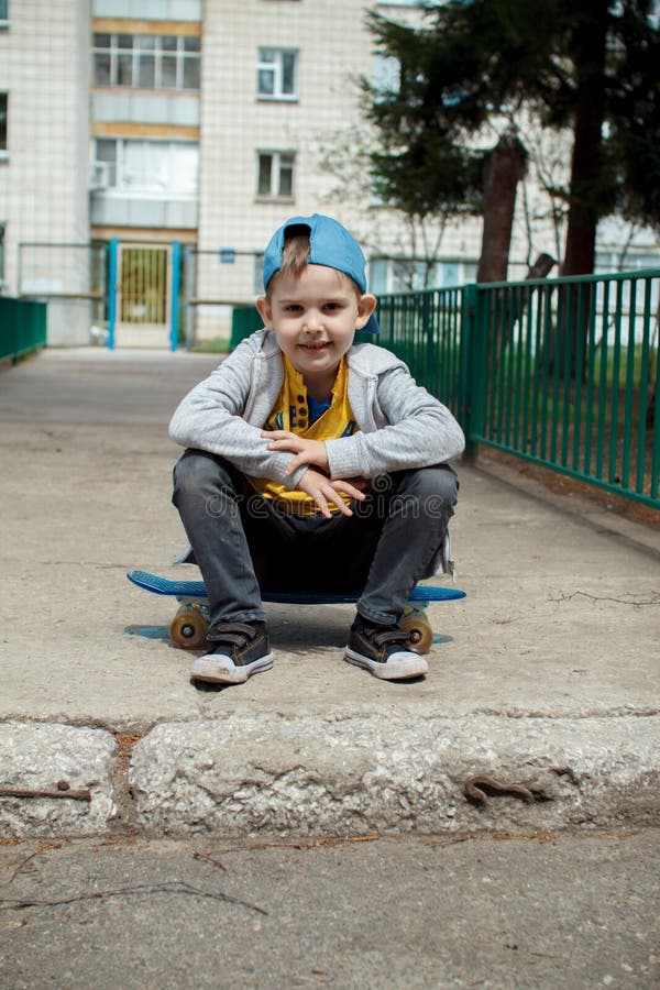 Little city boy with a skateboard. Young guy in a cap sits. Urban style. City kids. Kid`s having fun stock photo Little city boy with a skateboard. Young guy in a cap sits. Urban style. City kids. Kid`s having fun stock photo