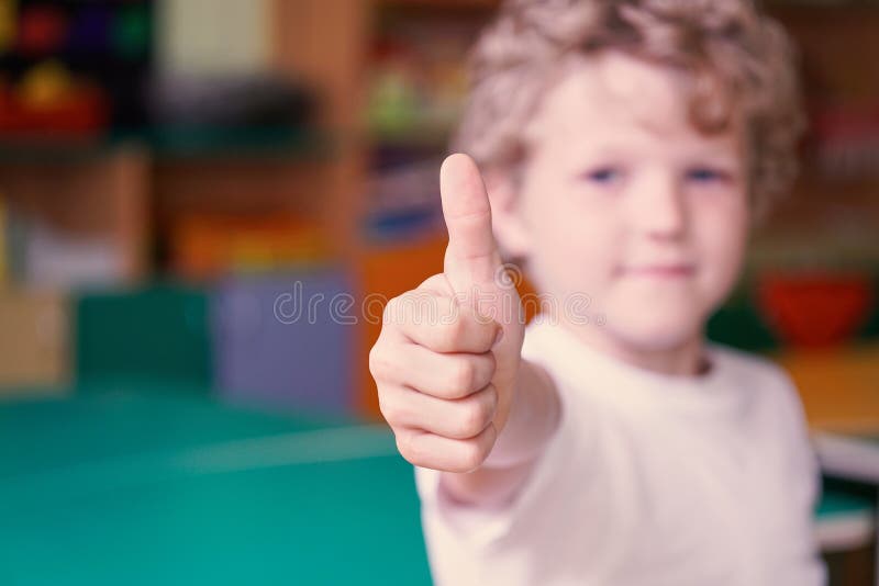 Little curly boy show his thumb up. Image with depth of field.