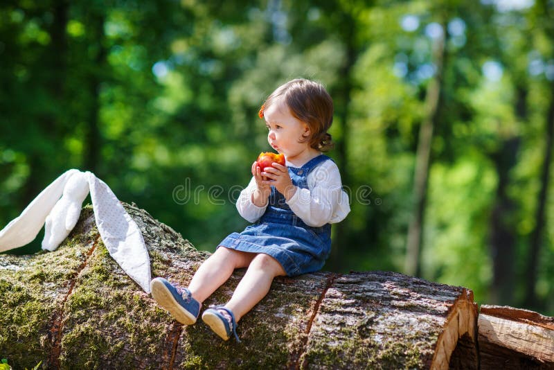 Little cute baby girl eating fruit in forest
