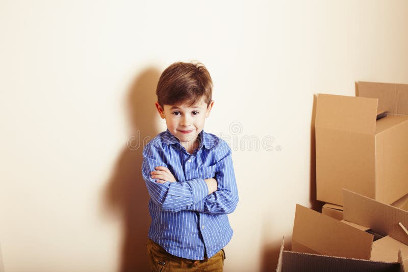Little cute boy in empty room, move to new house. home alone among boxes close up kid smiling, lifestyle real people