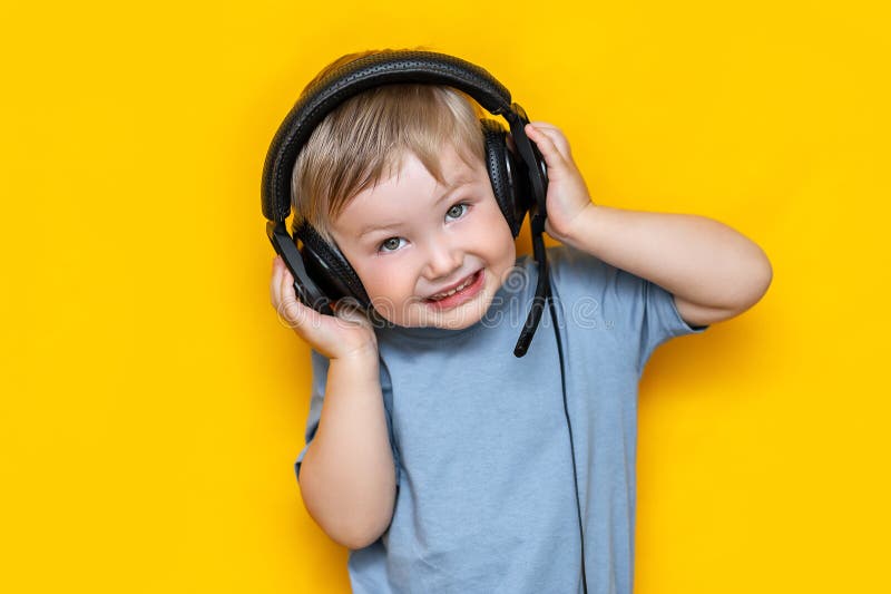 Little cute caucasian blonde boy in headphones posing happy smiling isolated on yellow background