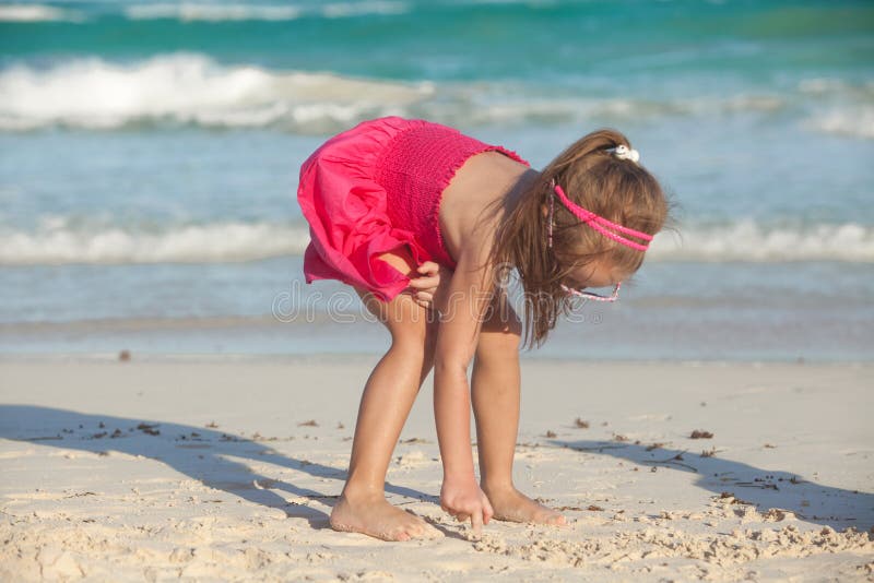 Little cute girl draws on the white sand at