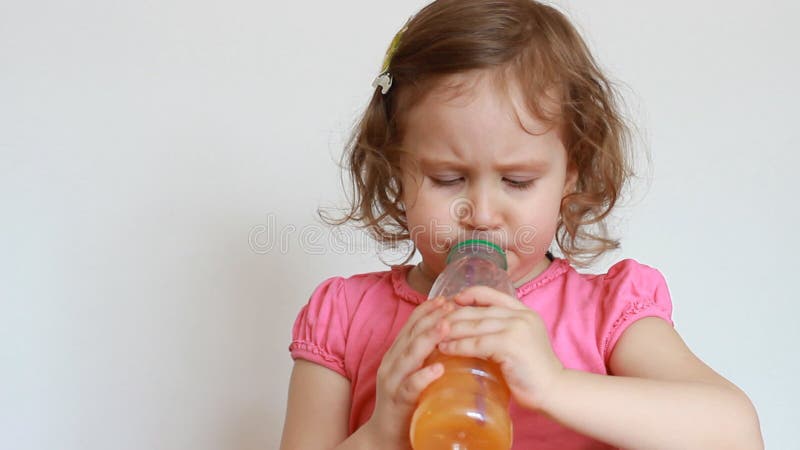 Little cute girl drinks orange drink from a bottle. Baby and freshly squeezed juice, smoothies, lemonade, fresh