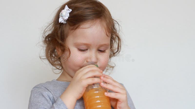 Little cute girl drinks orange drink from a bottle. Baby and freshly squeezed juice, smoothies, lemonade, fresh