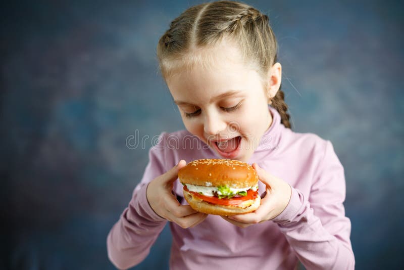Little cute girl eating a Burger in a cafe, concept of a children`s fast food meal stock photos Little cute girl eating a Burger in a cafe, concept of a children`s fast food meal stock photos