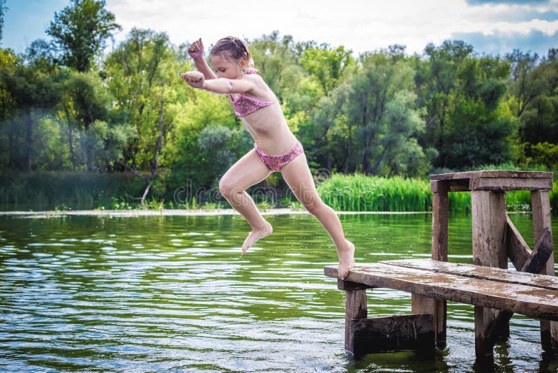 Little cute girl jumping off the dock into a beautiful river at sunset