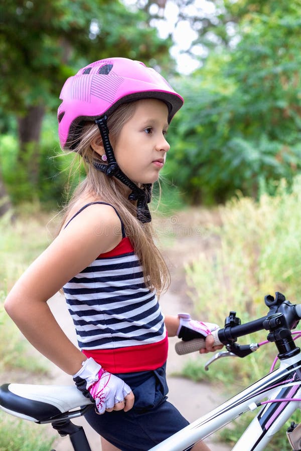 Little cute girl in a pink helmet near a bicycle