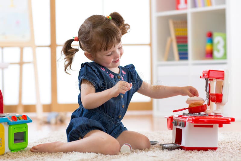 Little cute girl playing with utensil toys. Toddler kid in a playroom. Kid sitting on floor and cook in toy kitchen.