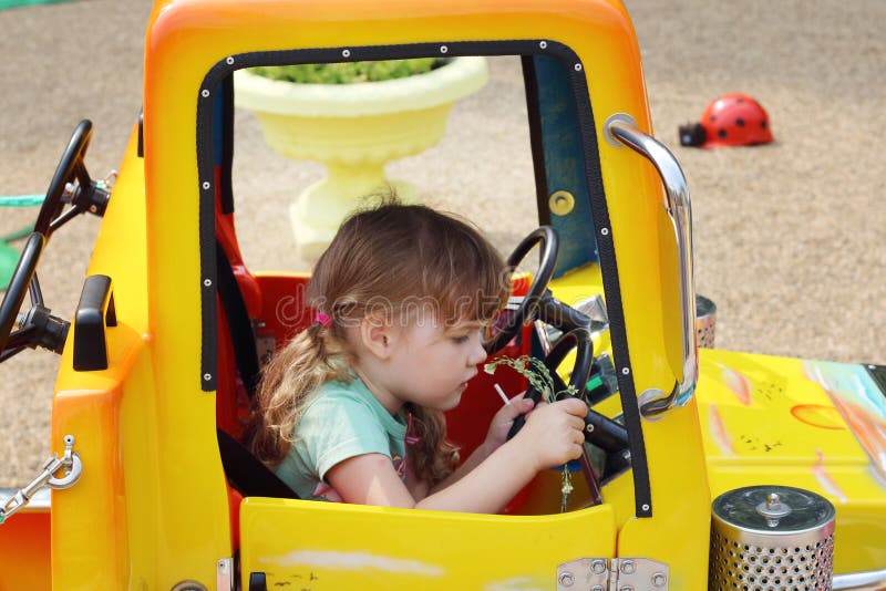 Little cute girl sits at wheel of big yellow toy car