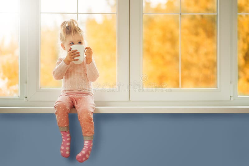 Little cute Kid Girl sitting by window holding cup of hot drink cocoa enjoying autumn forest background. Season Beauty fashion royalty free stock photos Little cute Kid Girl sitting by window holding cup of hot drink cocoa enjoying autumn forest background. Season Beauty fashion royalty free stock photos