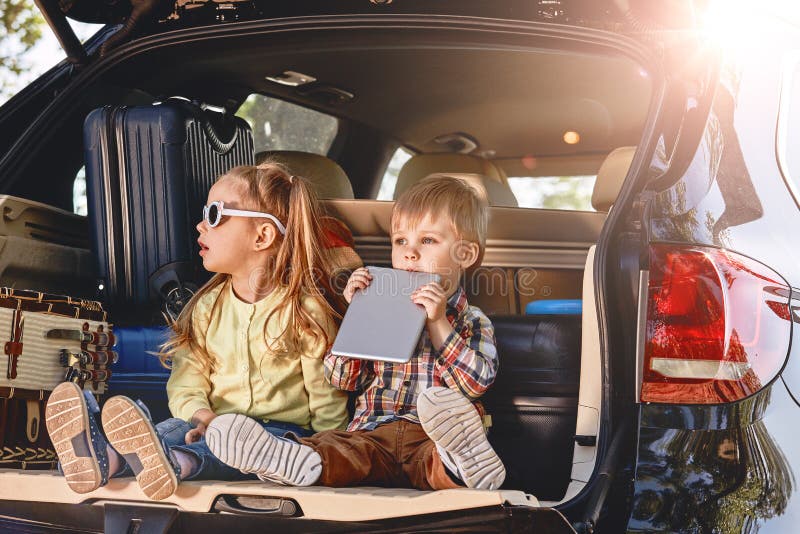 Little cute kids having fun in the trunk of a car with suitcases. Family road trip