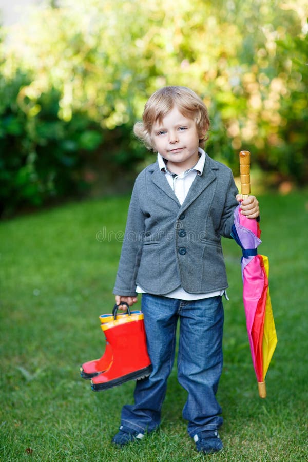 Little cute toddler boy with colorful umbrella and boots, outdoors