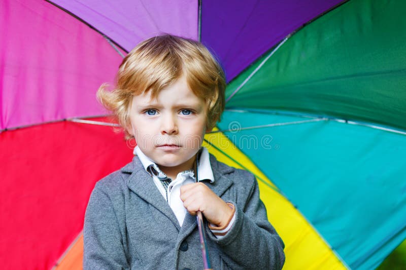 Little cute toddler boy with colorful umbrella and boots, outdoors