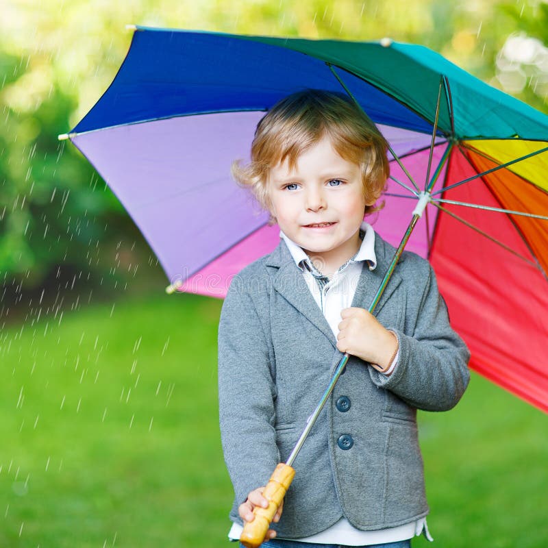 Little cute toddler boy with colorful umbrella and boots, outdoors