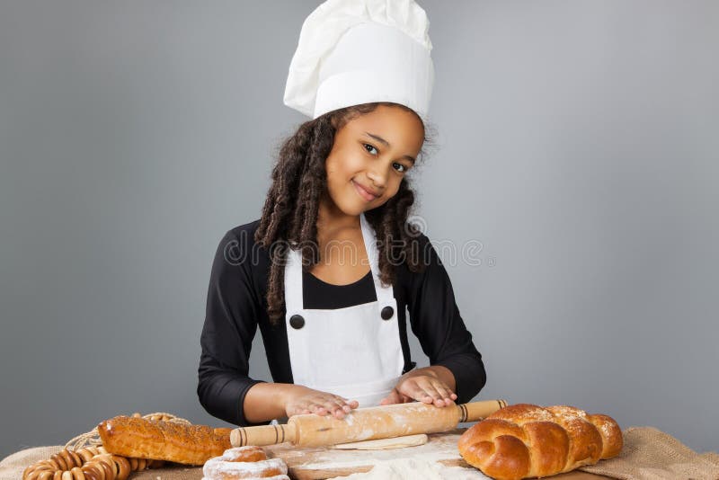 Little dark-skinned girl rolls the dough. The child learns to cook. Clothing and chef hat