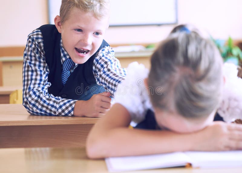 Little elementary school student boy tries to disturb the girl during the lesson. Boy tries to reach the girl`s back