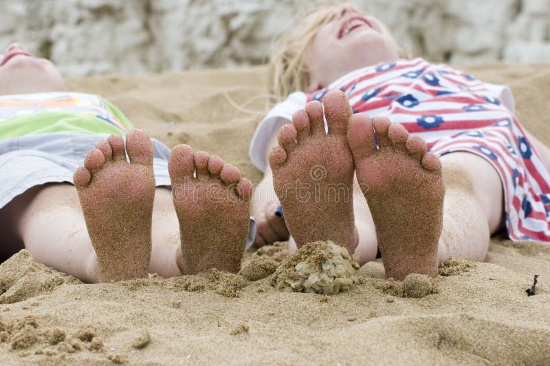 two children lying on the beach showing the soles of their sandy feet. two children lying on the beach showing the soles of their sandy feet.