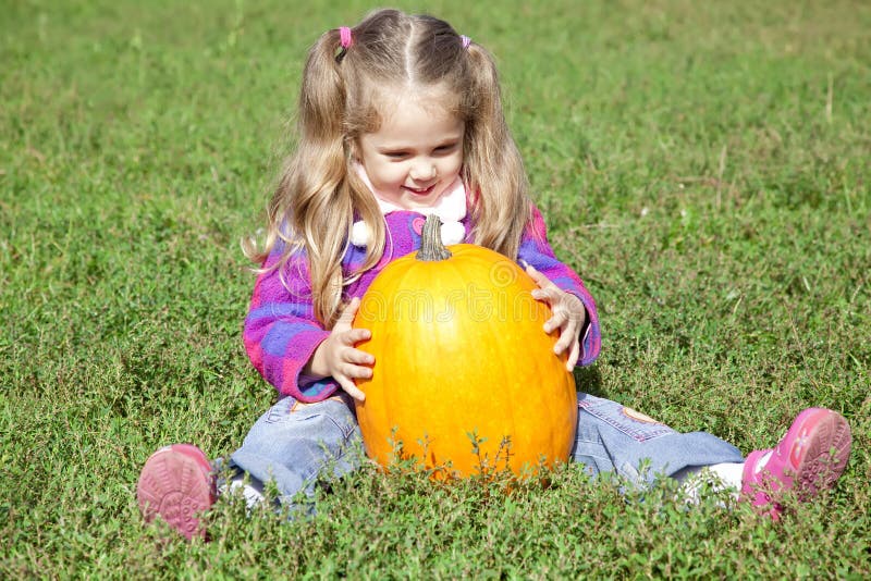 Little gardener girl with pumpkin at green grass