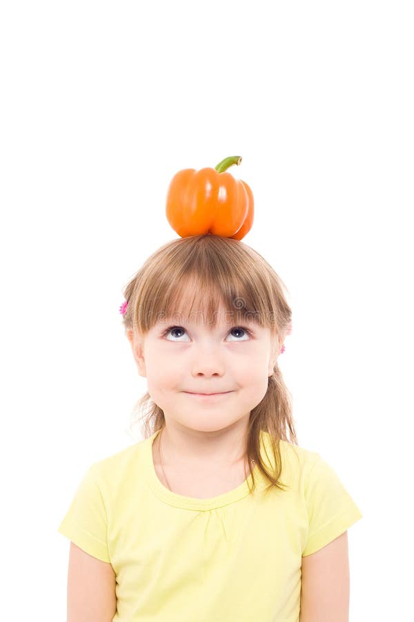 The portrait of a cute little girl holding an orange pepper on her head