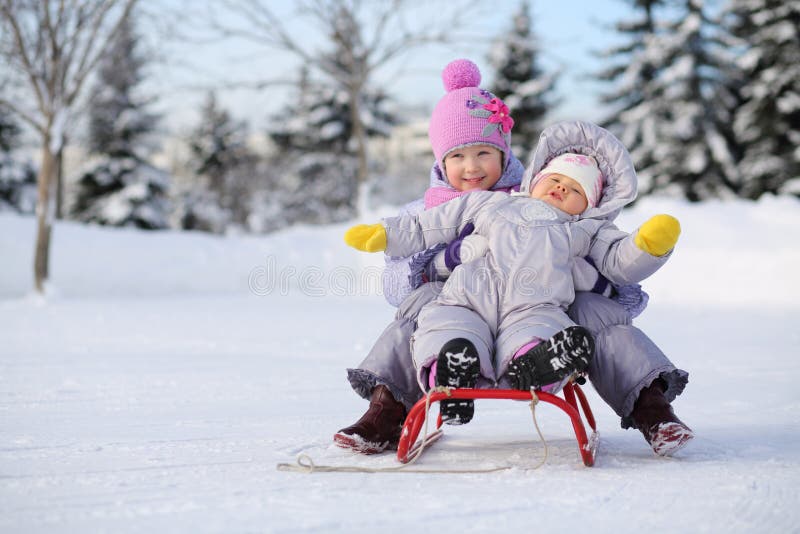 Little girl and baby dressed near forest sit on red sled