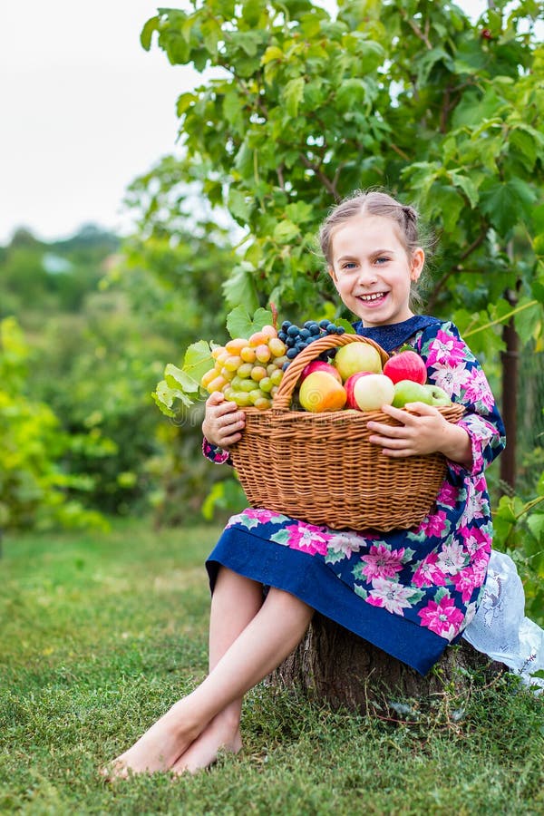 A little girl with a basket, with red apples and grapes