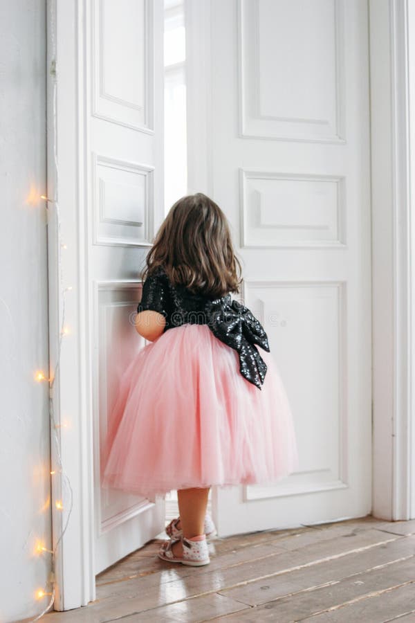 Little girl in beautiful pink dress with tutu skirt looks at door