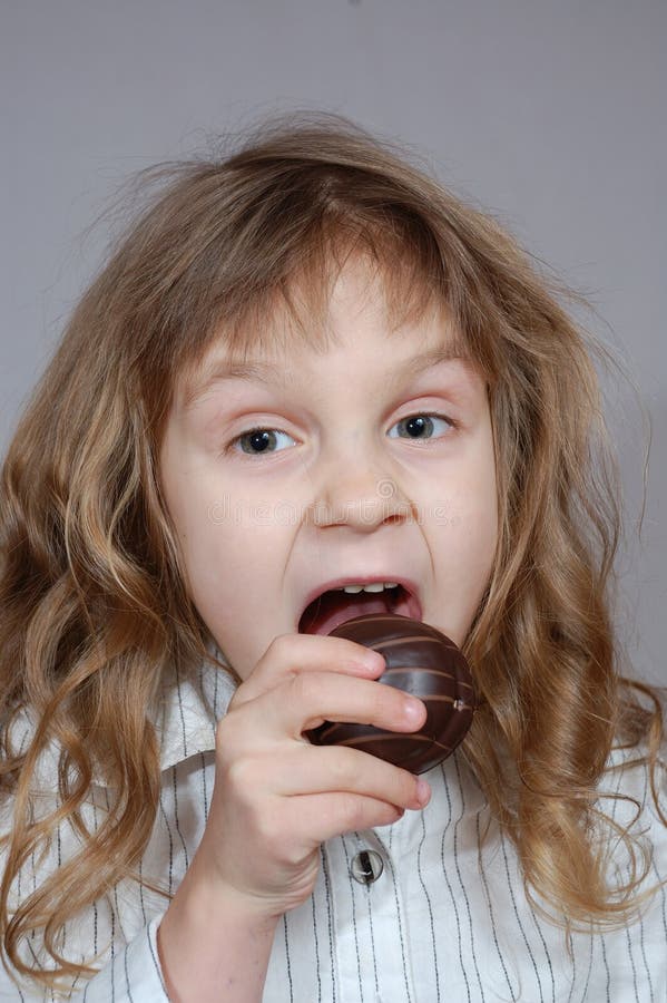 A little girl biting chocolate coated cookie.