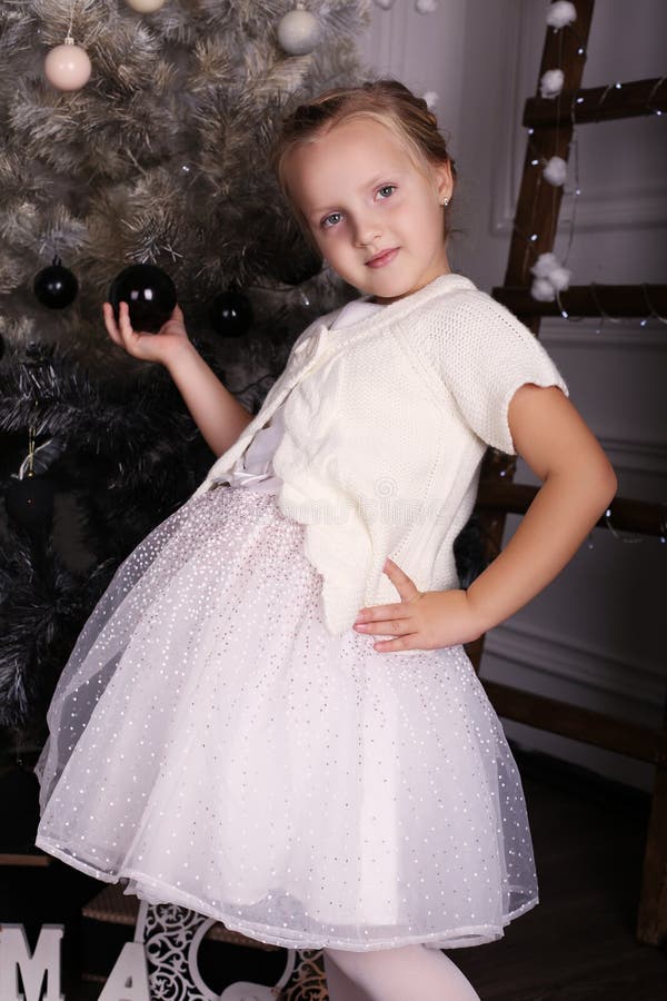 Little girl with blond hair wear elegant dress,posing beside Christmas tree