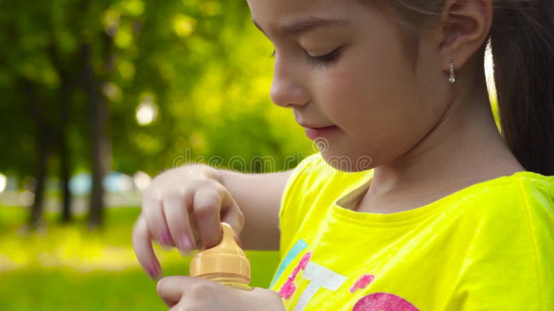 Little girl blowing soap bubbles in park. Closeup video