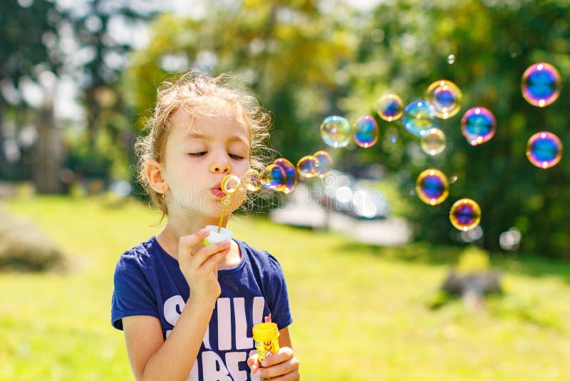 A little girl blowing soap bubbles in summer park.