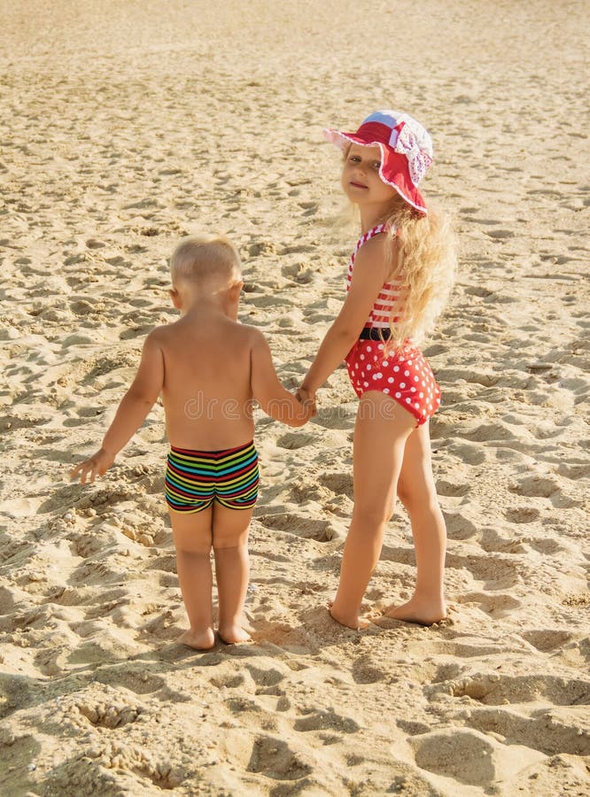 Little girl and boy are walking along beach, holding hands