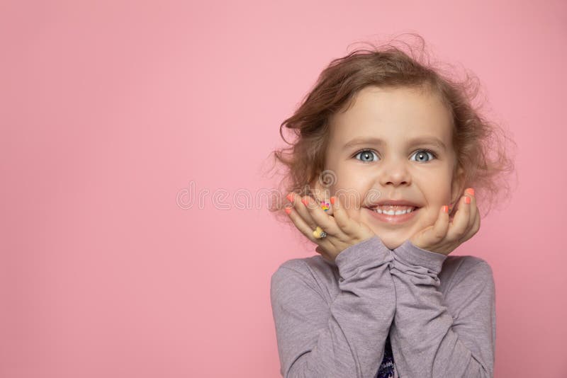 Little girl child blonde with curly girl painted her fingers with nail polish, look into frame in studio and smile. Close-up photo