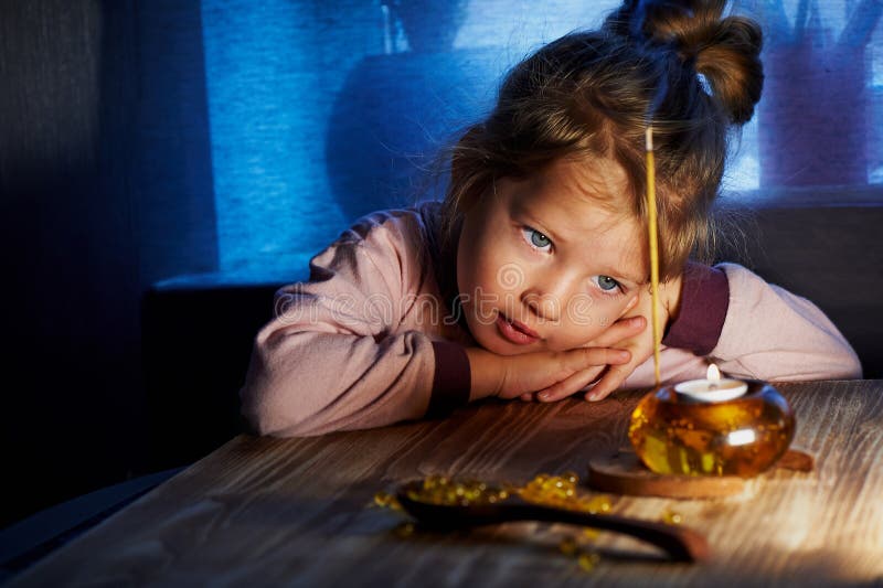 Little girl of 3 children looking at something like lit candle in candlestick. Home warmth and comfort as child