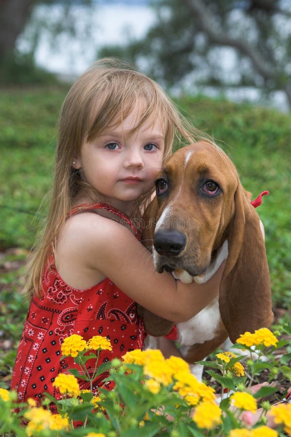 Portrait of little girl with pet basset hound in flower bed, shallow focus. Portrait of little girl with pet basset hound in flower bed, shallow focus