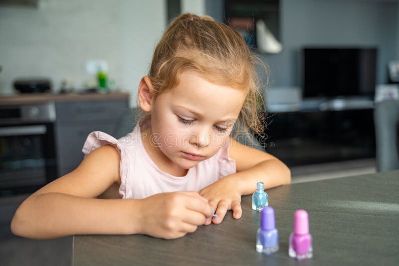 Little girl doing manicure and painting nails with colorful pink, blue and purple nail polish at home.