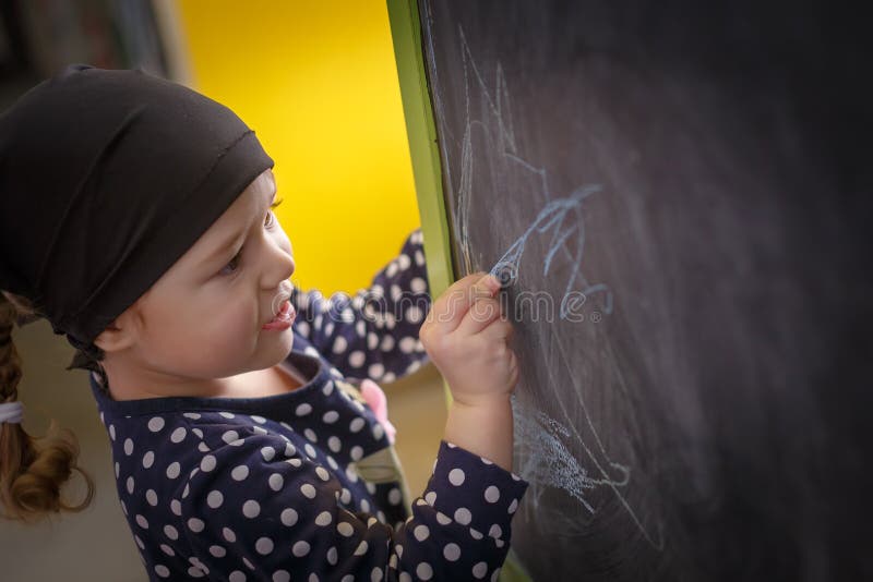 Little girl is drawing with blue chalk on a blackboard royalty free stock photography Little girl is drawing with blue chalk on a blackboard royalty free stock photography