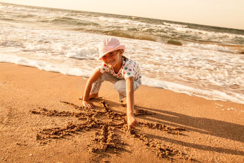 Little girl draws sun on sand at the beach