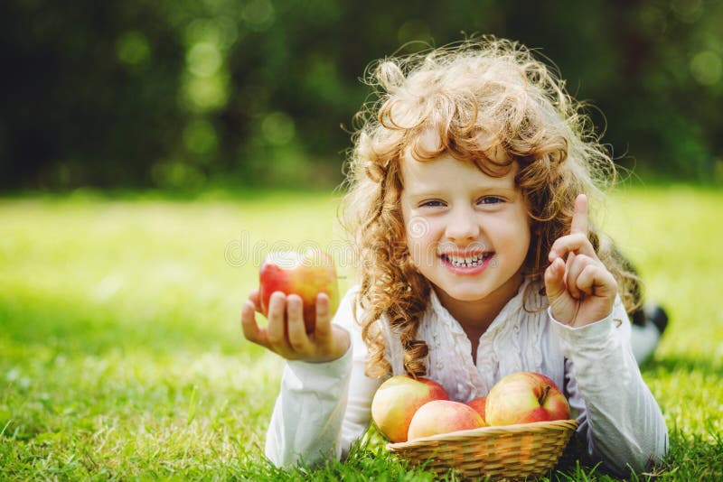 Little girl is eating apple and smiling showing white teeth.