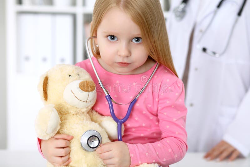 Little girl examining her Teddy bear by stethoscope. Health care, child-patient trust concept. Clinic, doctor.