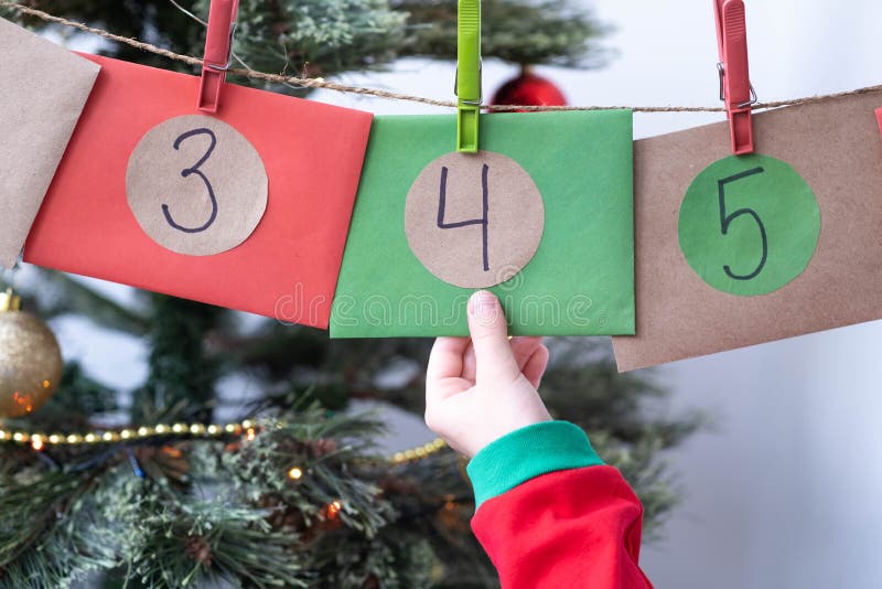 Little girl hand taking envelope numbered 4 of homemade Advent calendar near Christmas tree. Selective focus stock photography
