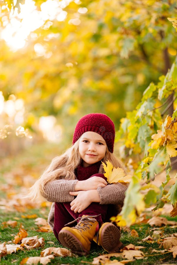 Little Girl in Hat Sitting Under Trees in Autumn Park with Maple Leaf ...