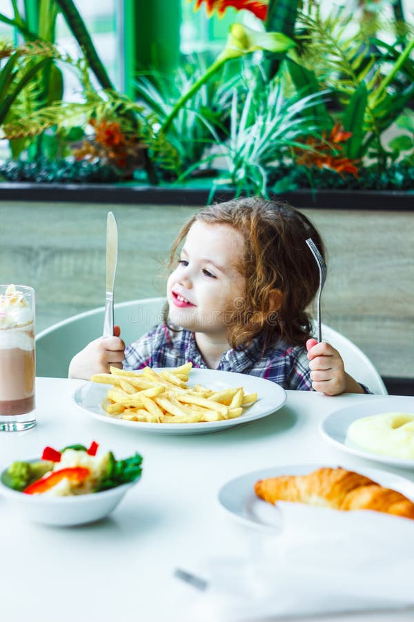 Little Girl Having Lunch in the Restaurant with the Table Knife and