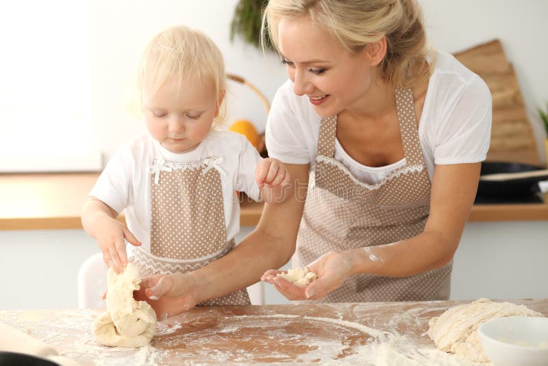 Little girl and her blonde mom in beige aprons playing and laughing while kneading the dough in kitchen. Homemade pastry royalty free stock photo Little girl and her blonde mom in beige aprons playing and laughing while kneading the dough in kitchen. Homemade pastry royalty free stock photo