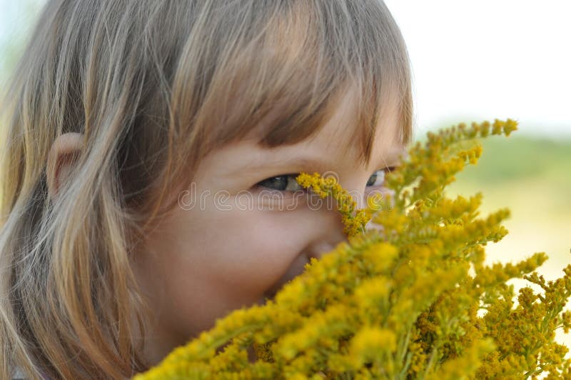 A little girl holding a bouquet of field summer flowers and smelling it with her eyes closed