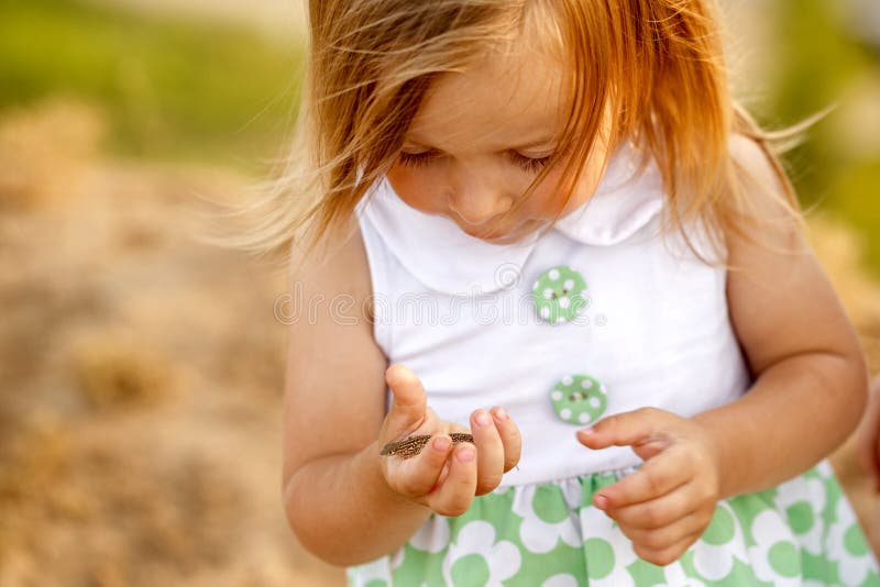 Little girl holding her hand on the small green lizard.