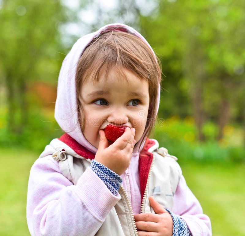 Little girl in a hoodie eating strawberries stock photos Little girl in a hoodie eating strawberries stock photos